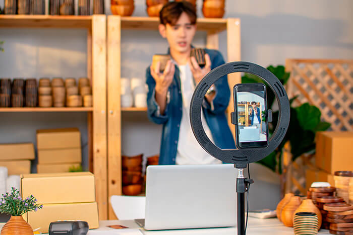 homem de origem asiática gravando um vídeo para o tiktok, usando ring light e celular, mostrando alguns produtos para casa