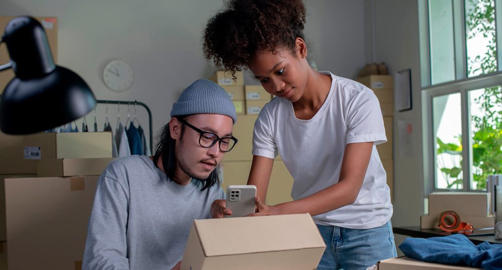 homem e mulher usando um celular para ler uma etiqueta de envio colada em uma caixa de papelão