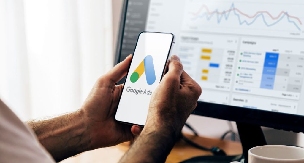 Mãos segurando um celular com o aplicativo do google ads.
