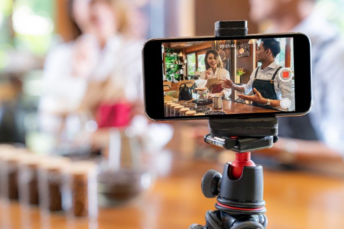 Um celular, em um tripé, gravando duas pessoas.