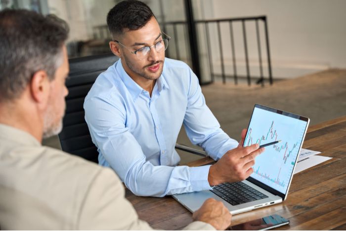 Dois homens fazendo reunião, com um computador mostrando um gráfico.
