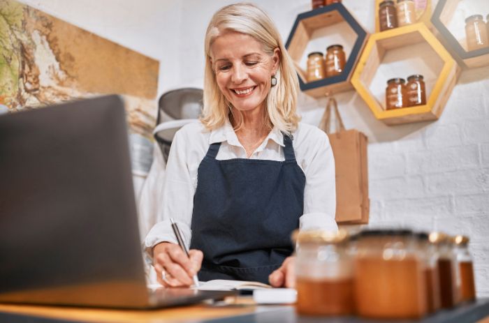 Mulher no computador sorrindo e fazendo anotações.