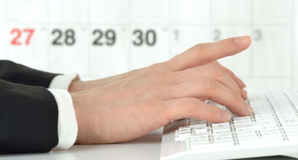 Homem no computador com calendário de fundo, consultando sobre prazo de entrega.