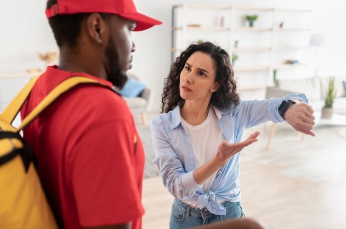 Mulher mostrando relógio para entregador, para reclamar do atraso na entrega de produto.
