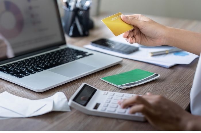 Pessoa em uma mesa com calculadora, notebook e cartão crédito.