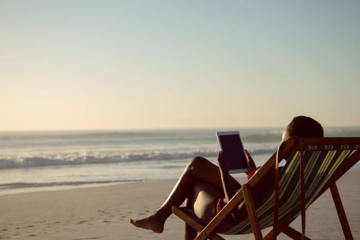 Mulher na praia sentada com tablet na mão