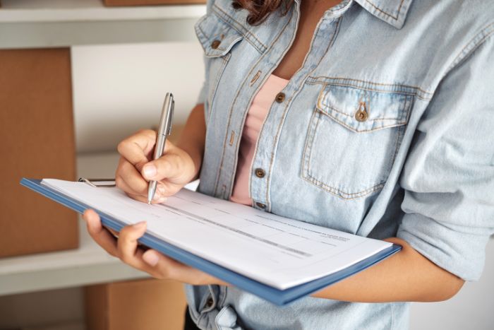 Mulher com prancheta na mão escrevendo, organizando.